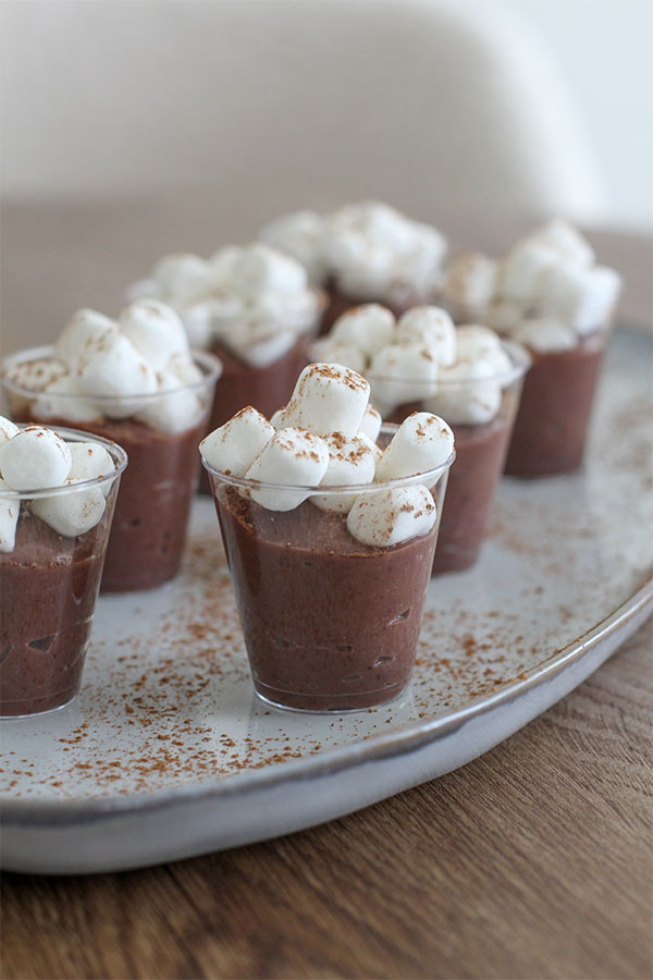 Mini clear cups filled with chocolate pudding, topped generously with mini marshmallows and a dusting of cocoa powder, arranged on a serving tray