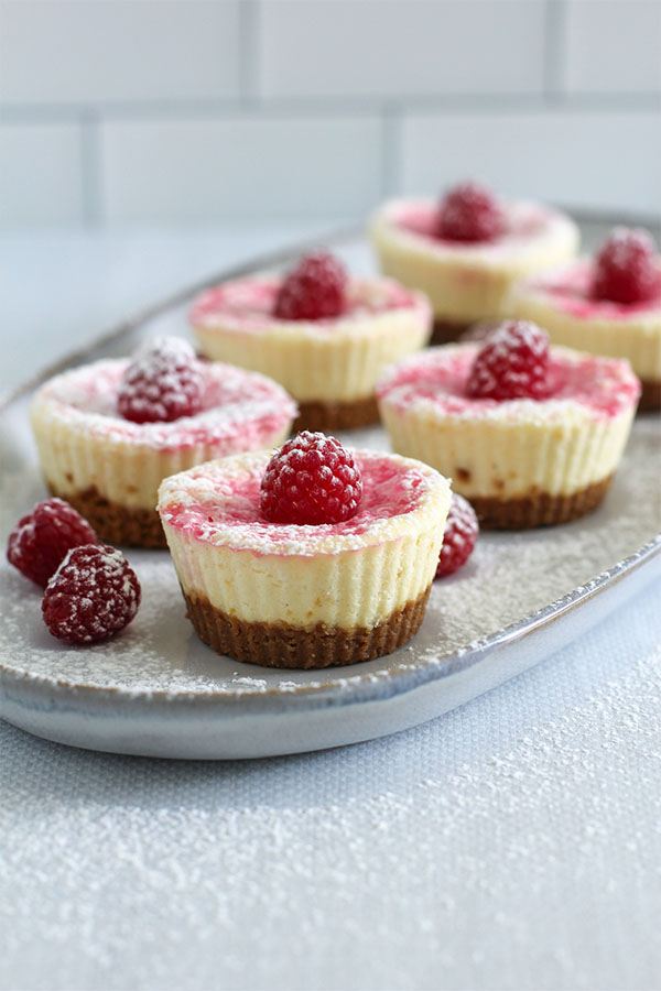 A slightly tilted perspective of the plated cheesecakes, emphasizing their height, creamy texture, and crunchy graham cracker crust