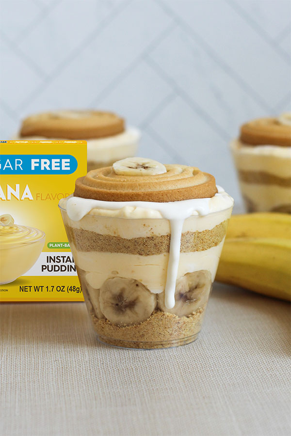 Individual serving of banana pudding in a clear cup with cool whip and cookie garnish