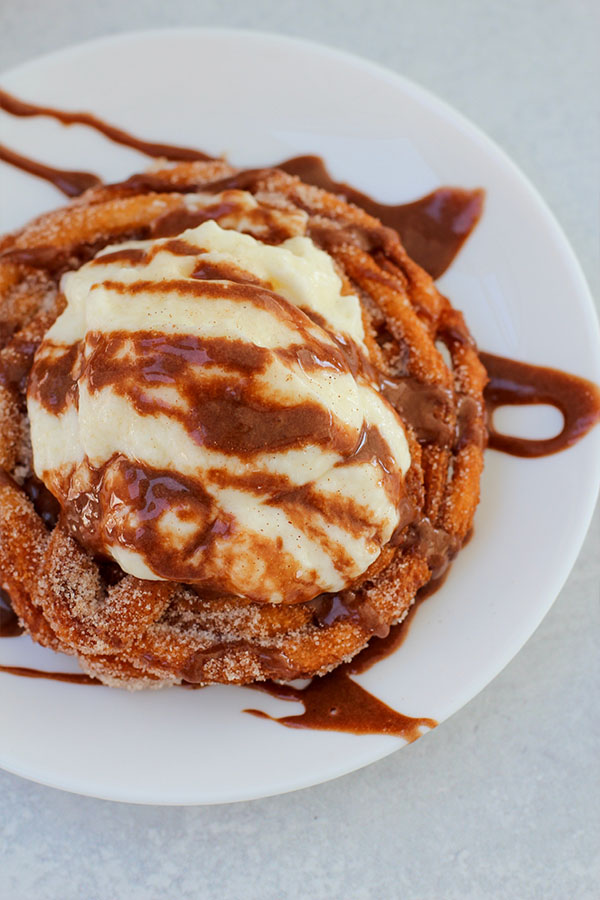 Overhead view of churro sundae topped with vanilla pudding and chocolate drizzle on a white plate