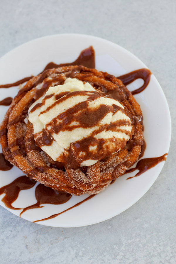 Top-down shot of cinnamon sugar churro spiral topped with vanilla pudding and chocolate sauce