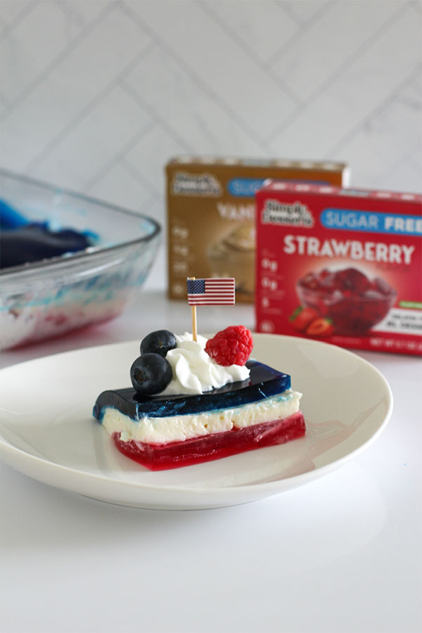 Side view of a festive layered pudding and jel square topped with whipped cream, fresh berries, and a small United states flag for 4th of july