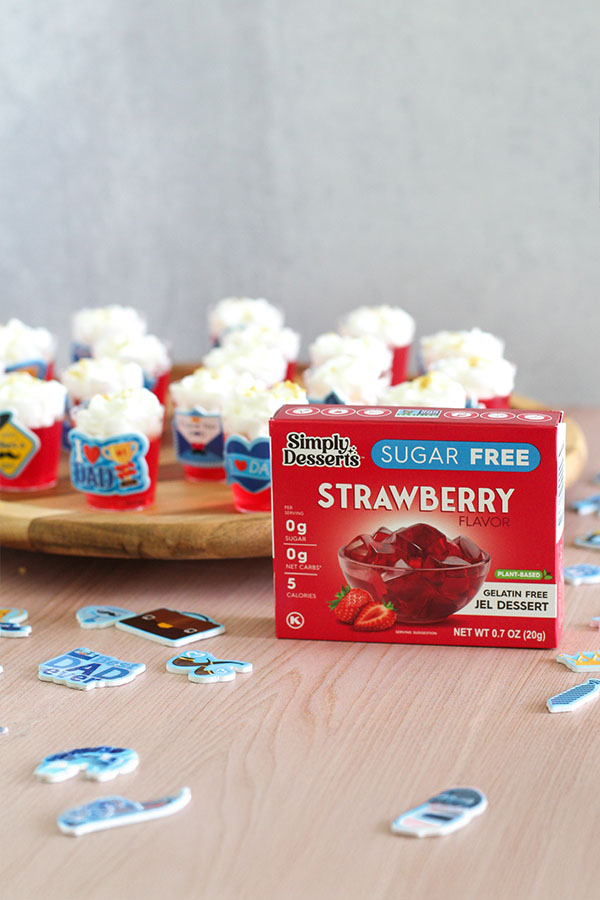Sugar-free strawberry jel shots topped with whipped cream in red cups decorated with Father's Day stickers, Simply Desserts box in foreground