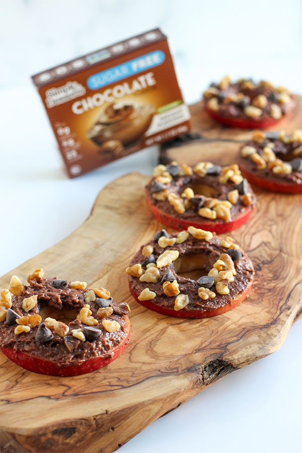 Red apple ring topped with sugar-free chocolate pudding, chopped walnuts, and chocolate chips on a wooden serving board