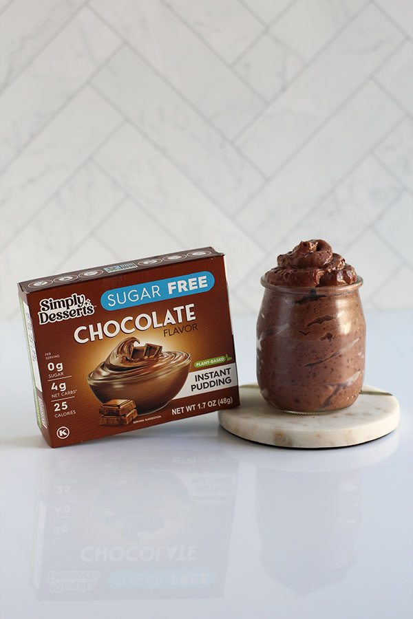 Simply Desserts Sugar Free Chocolate Pudding box with a jar of prepared chocolate pudding on a marble coaster