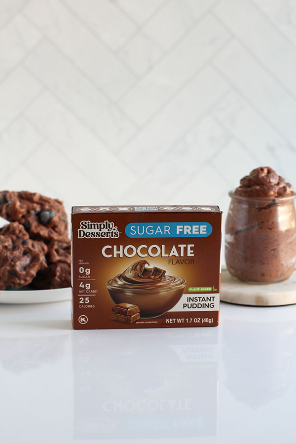 Simply Desserts Sugar Free Chocolate Pudding box displayed with frozen blueberry clusters and a jar of pudding in the background