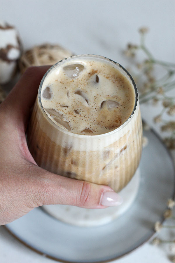 Hand holding a glass of iced pumpkin salted caramel pudding latte with ice cubes and foam on top