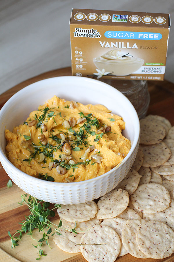 Bowl of savory pumpkin dip topped with walnuts and thyme, served with crackers and Simply Desserts Vanilla Pudding box