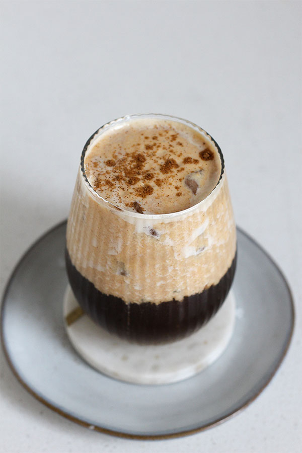 Close-up of pumpkin salted caramel pudding latte topped with pumpkin spice in a ribbed glass on a grey plate