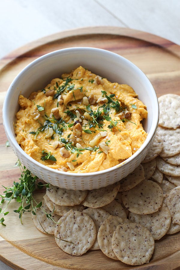 Overhead view of pumpkin dip in a white bowl surrounded by almond crackers
