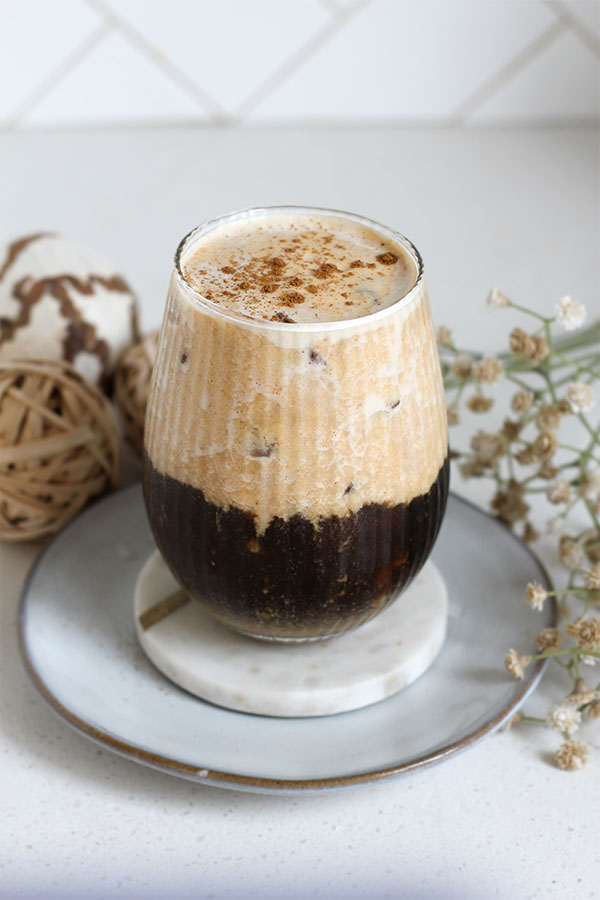 Pumpkin salted caramel pudding latte in a ribbed glass with layered cold brew and pumpkin foam, styled with dried flowers