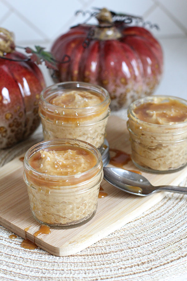 Three salted caramel pudding jars with caramel drizzle in front of decorative pumpkins