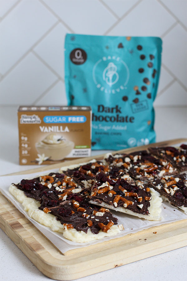 Chocolate pretzel bark set on a wooden cutting board with pretzels and cranberries sprinkled on top