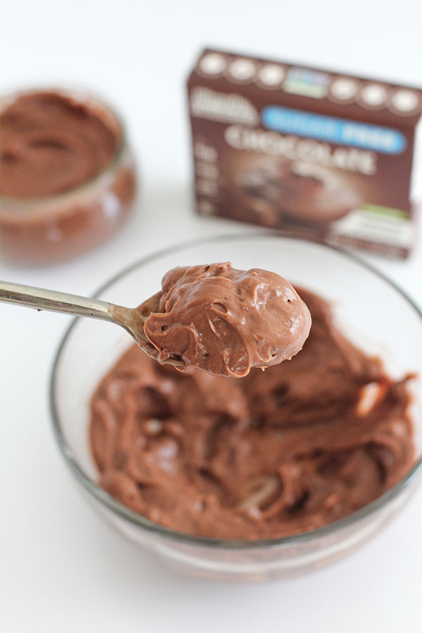 A spoonful of rich, smooth Simply Desserts Sugar-Free Chocolate Pudding held above a glass bowl of pudding