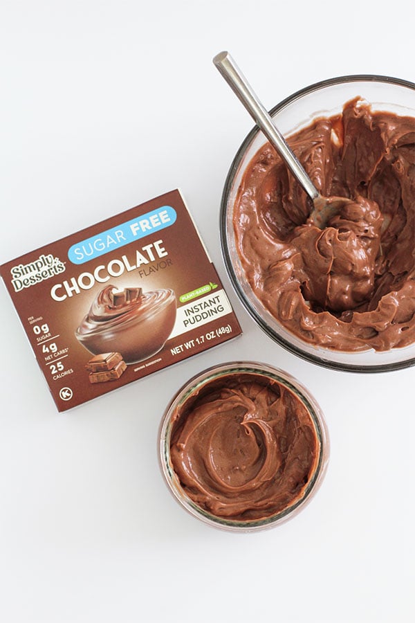 A top-down view of Simply Desserts Sugar-Free Chocolate Pudding box next to a large bowl and a small serving jar of chocolate pudding