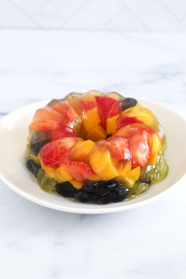 Fruity Jel Cake with layered mango, strawberries, blueberries, and grapes on a white plate
