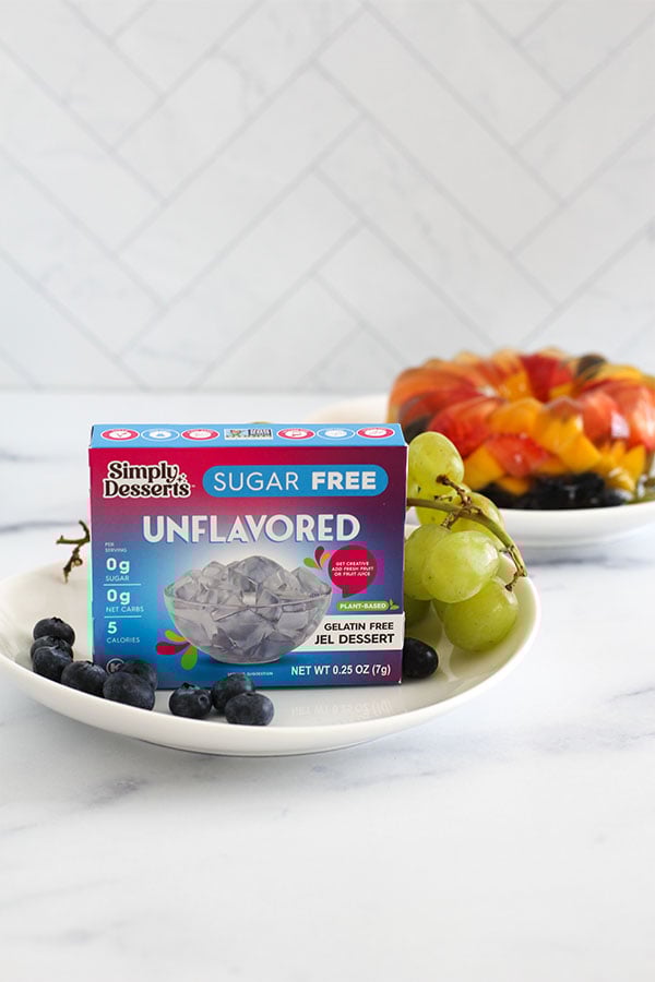 Simply Desserts Unflavored Jel Dessert box beside fresh fruit and the Fruity Jel Cake in the background