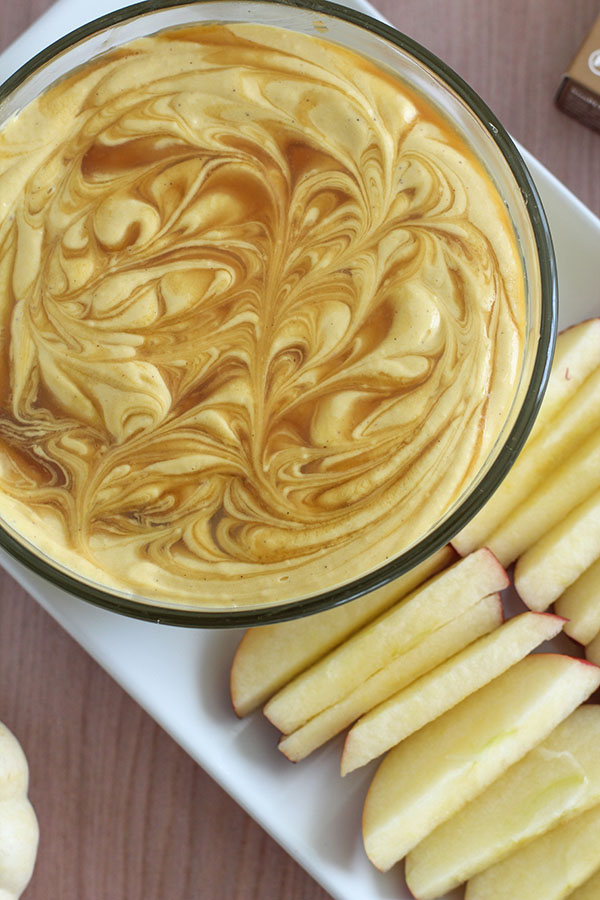 Overhead view of a bowl of pumpkin cheesecake dip surrounded by sliced apples for dipping
