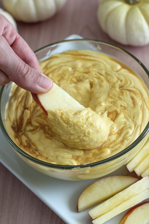 Hand dipping a fresh apple slice into thick pumpkin cheesecake dip made with sugar-free vanilla pudding