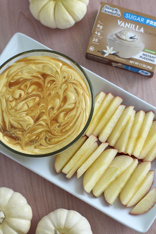 Overhead view of pumpkin cheesecake dip and apple slices next to a Simply Desserts Vanilla Pudding box on a wooden table