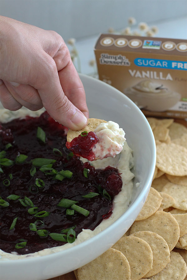 Hand dipping a cracker into the spicy cranberry jalapeño dip side view