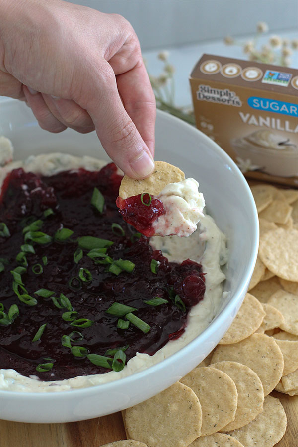 Hand dipping a cracker into the spicy cranberry jalapeño dip